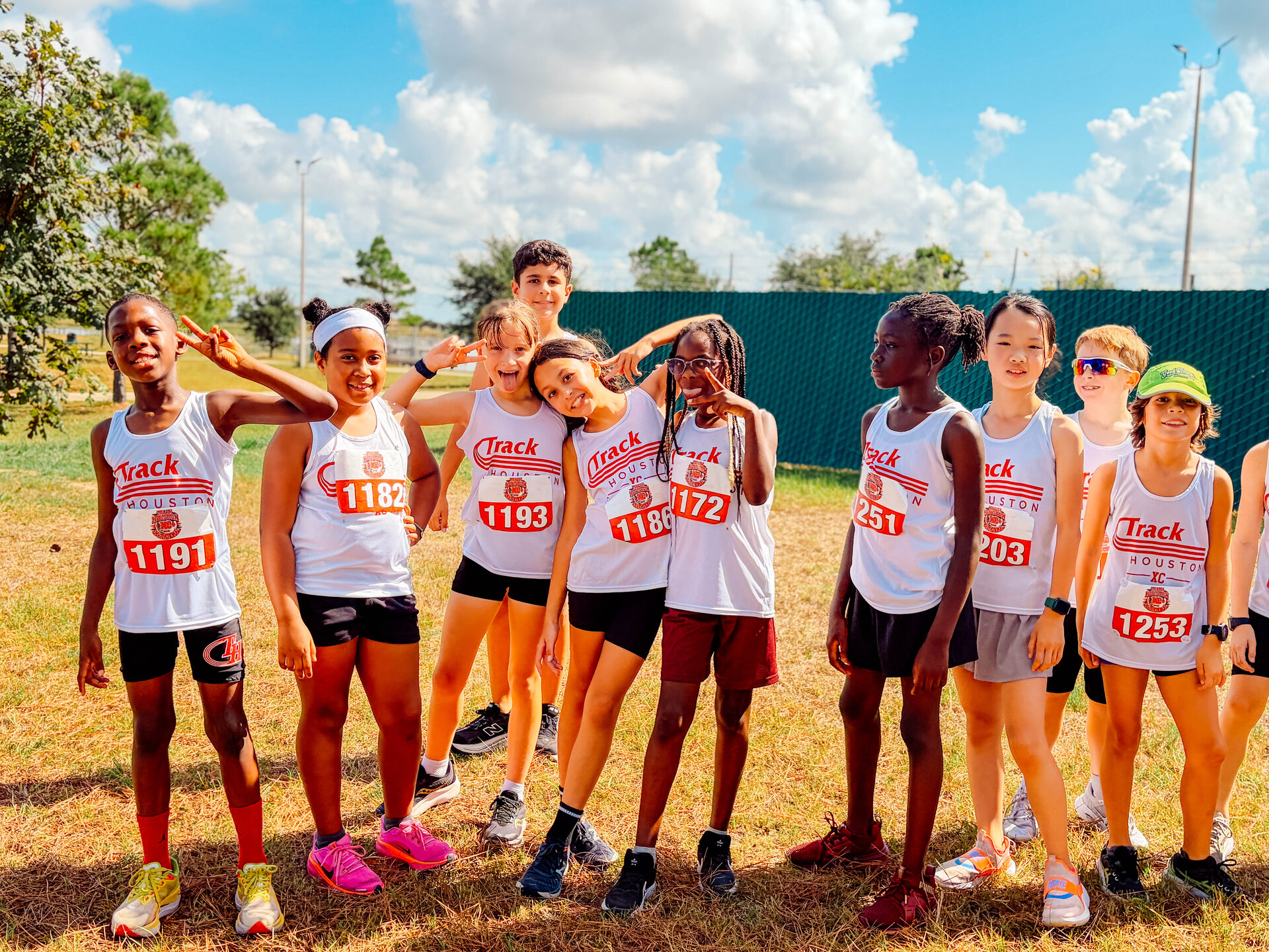 Track Houston cross country runners in race bibs flash peace signs on the course.